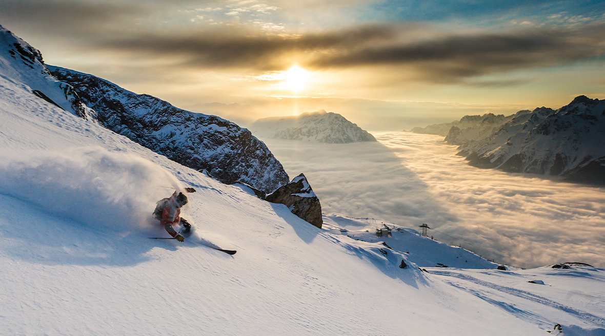 someone skiing down a mountain side as the sun sets in the far distance